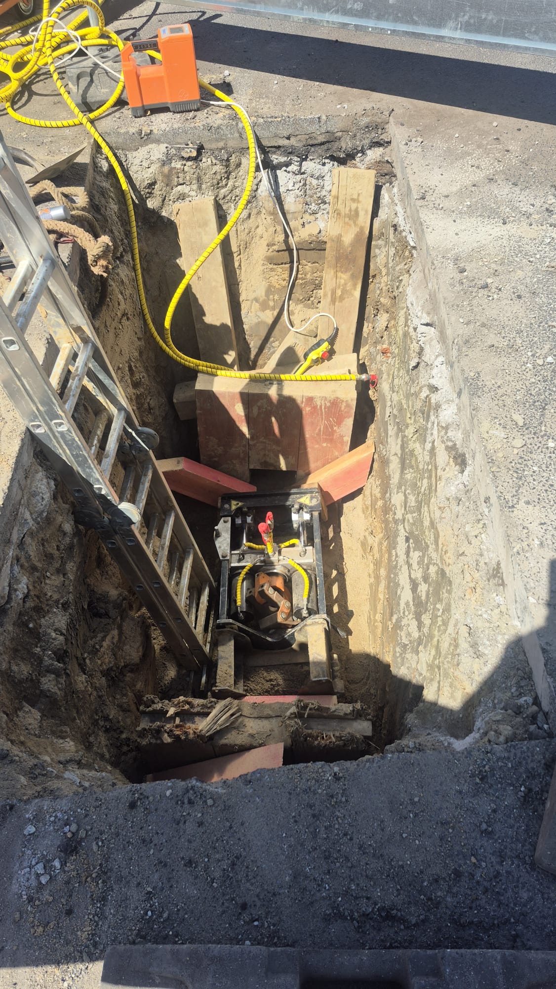 Drei Mitarbeiter in Warnwesten und Schutzhelmen montieren ein Solarmodul neben einer Straßenbaustelle mit einem Graben